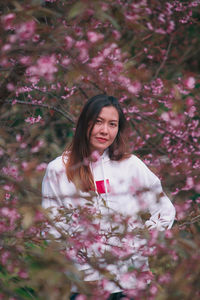 Portrait of beautiful young woman standing by pink flower tree