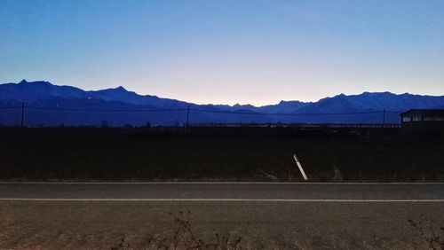 Road by silhouette mountains against clear sky