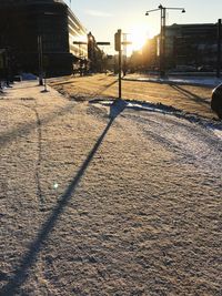 Snow covered street by buildings in city during sunset