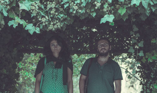 Portrait of a young man and woman standing against plants