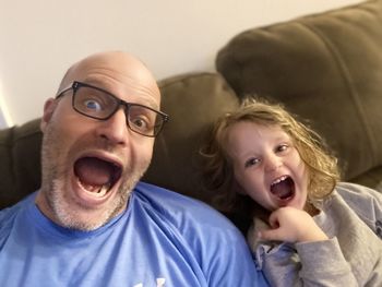 Portrait of father with daughter making face while sitting on sofa at home