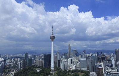 Communications tower in city against cloudy sky