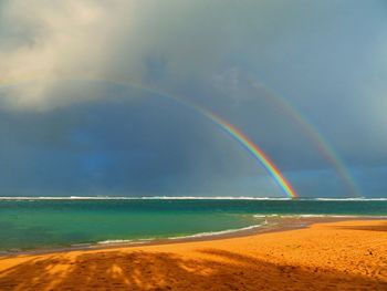 Scenic view of beach against rainbow in sky