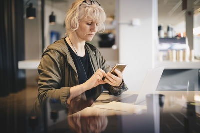 Businesswoman using smart phone while sitting at desk in office