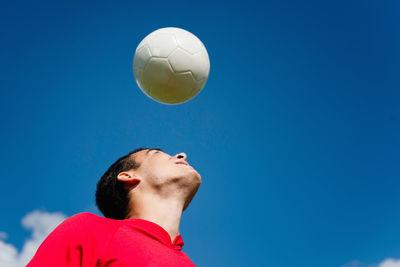 Low angle view of man playing soccer ball against blue sky
