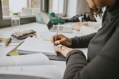 Midsection of mature female student writing in book while studying at university