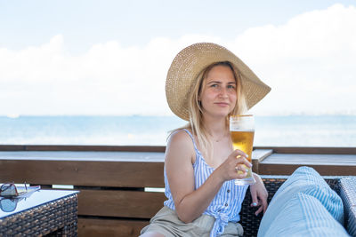 Portrait of woman holding beer against sea