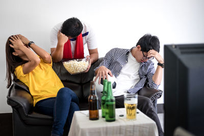 Sad fans sitting on couch during soccer match on tv