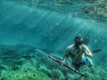 Shirtless man holding harpoon swimming undersea