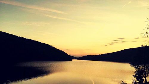 Scenic view of river by silhouette mountains against sky