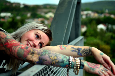 Smiling young woman with tattoo on hands leaning on metallic railing