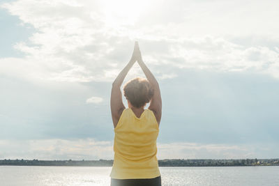 Rear view of woman standing by water against sky