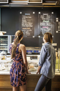 Friends reading menu on blackboard while standing at counter in cafe