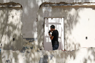 Man holding mobile phone while standing at demolished building