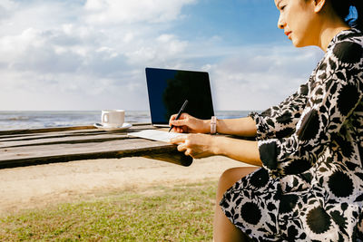 Side view of woman working on laptop computer at beach