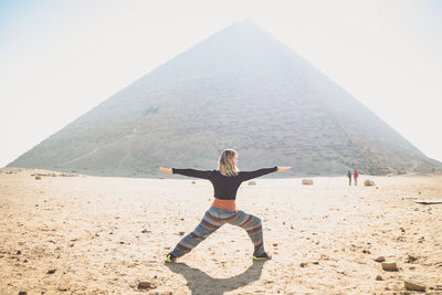 Full length of woman practicing yoga against pyramid at egypt