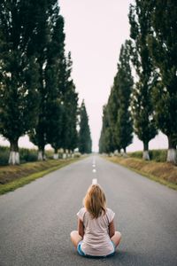 Rear view of girl sitting on road