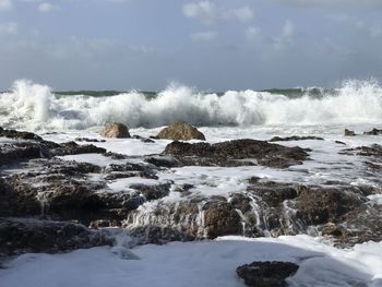 Waves splashing on rocks against sky