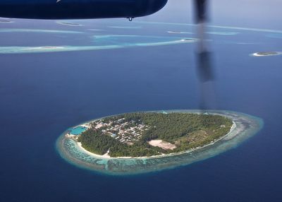 Cropped image of airplane flying over atoll in sea