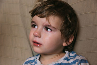 Portrait of a crying boy sitting on a sofa.