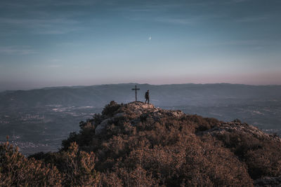 Man standing by cross on mountain against sky during sunset