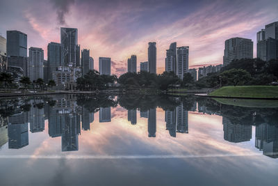 Reflection of trees in city against sky during sunset