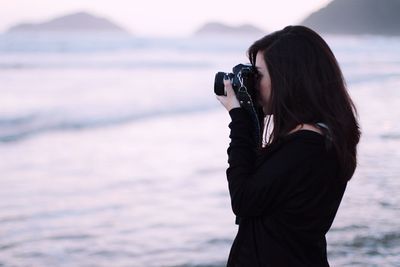 Side view of woman photographing from slr camera against sea