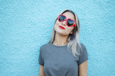 Portrait of woman wearing sunglasses and red lipstick against wall