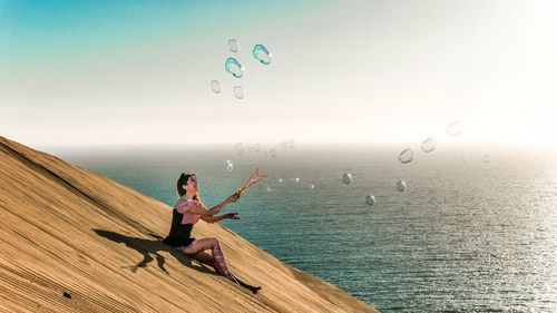 Full length of woman sitting in sea against sky