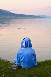 Man sitting on grass by lake against sky