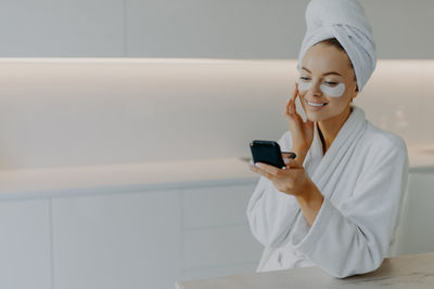 Woman holding mobile phone while sitting on laptop