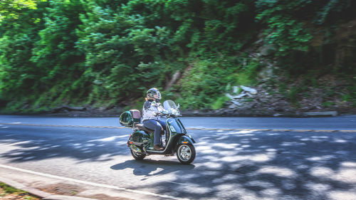 Man riding motorcycle on road against trees