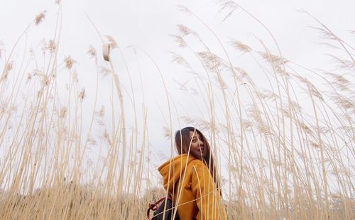 Low angle portrait of smiling mid adult woman standing amidst plants against sky