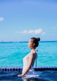 Woman sitting in swimming pool against sea