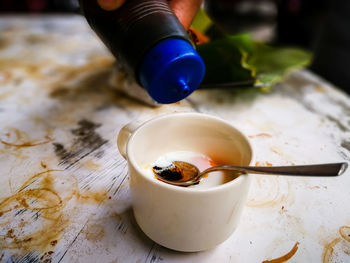 Half boiled eggs with soy sauce and pepper served in a cup on a stained table.