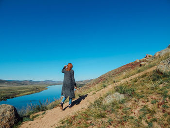 Rear view of woman walking on mountain against clear blue sky