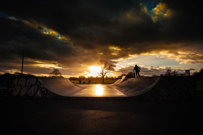 Man standing at skateboard park against sky during sunset