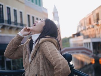 Happy young woman laughing while standing against building in city