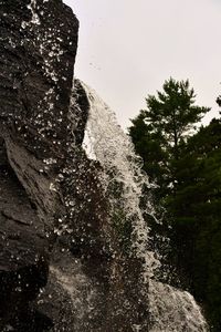 Low angle view of waterfall amidst rocks against sky