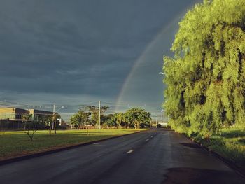 Road by trees and rainbow against sky