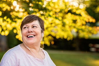 Portrait of happy smiling senior plus size woman with earphones enjoying music in park outdoors 