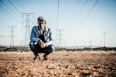 Portrait of man squatting under electricity pylons