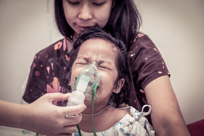 Cropped image of doctor putting mask on crying girl