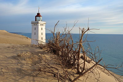 Lighthouse by sea against cloudy sky