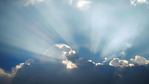 Low angle view of sunlight streaming through clouds