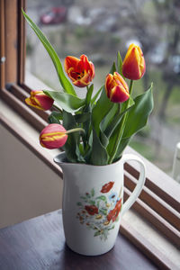 A white porcelain jug with flower print containing a bouquet of red and yellow tulips.