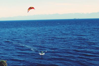 Person paragliding in sea against sky