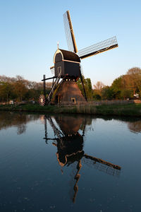 Traditional windmill by lake against sky