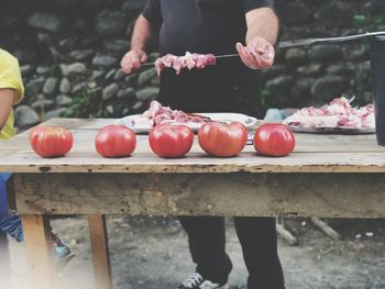 Midsection of man putting meat in skewer while standing against wall