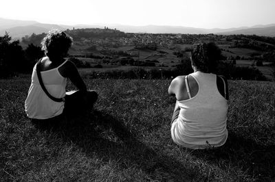 Rear view of women sitting on field against sky